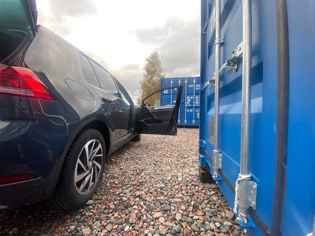 close up view of a car with door and boot open parked next to a shipping container