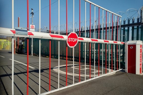 A red and white barrier gate with a "STOP" sign, on a entrance to a storage facility.