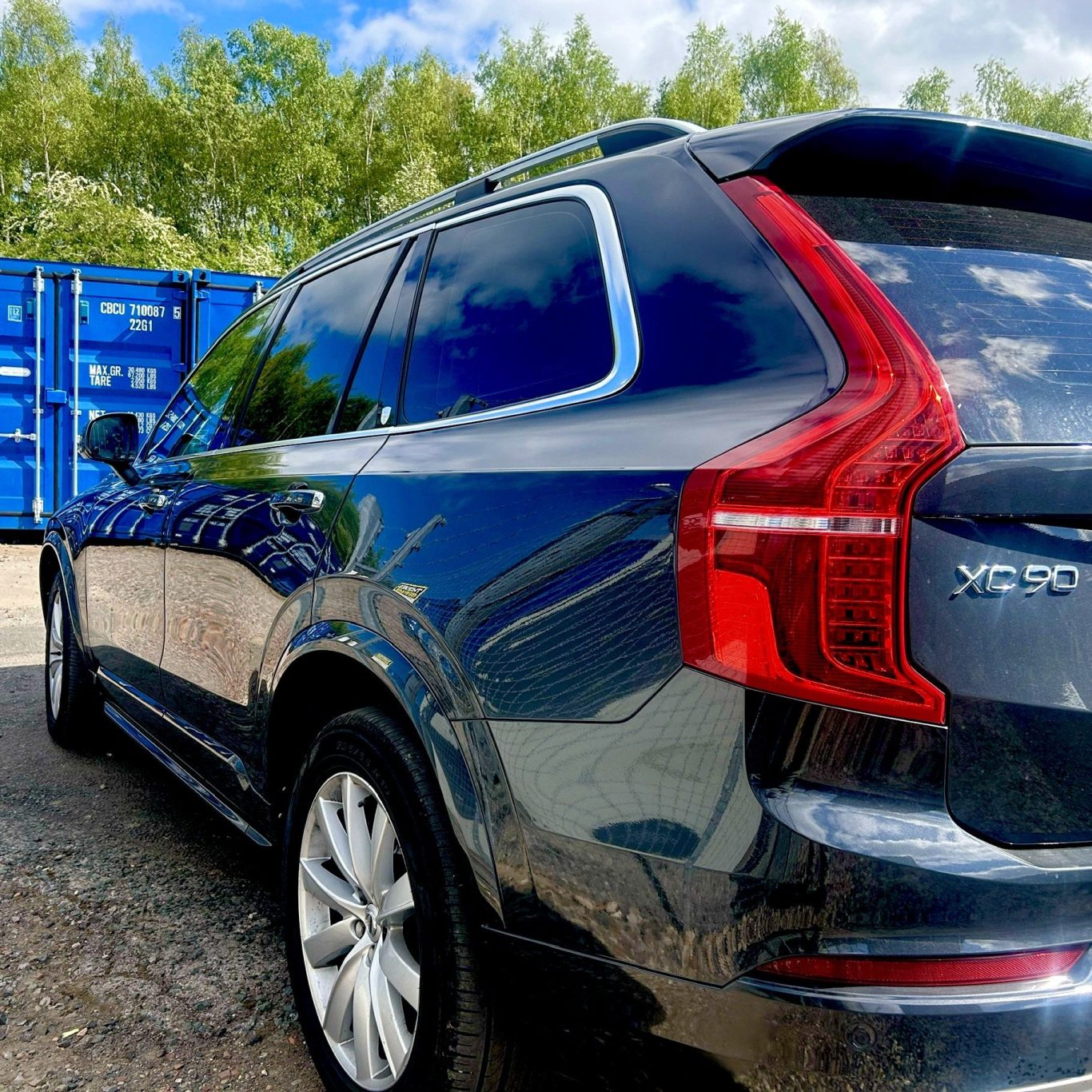 car on self storage facility Side view of a grey Volvo XC90 parked near shipping containers.