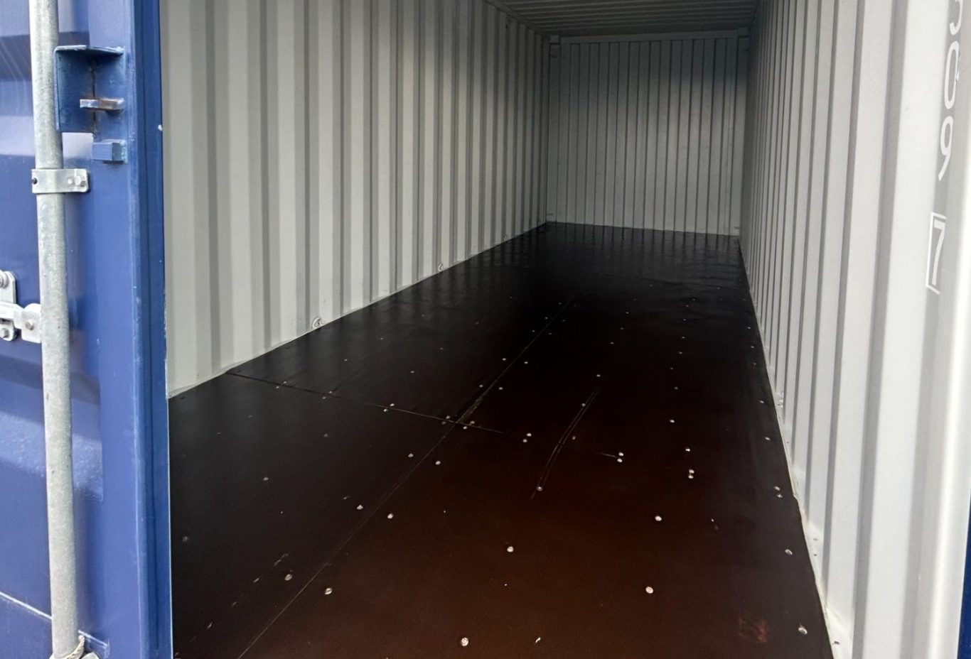 Empty shipping container interior, featuring metal walls and a brown floor.