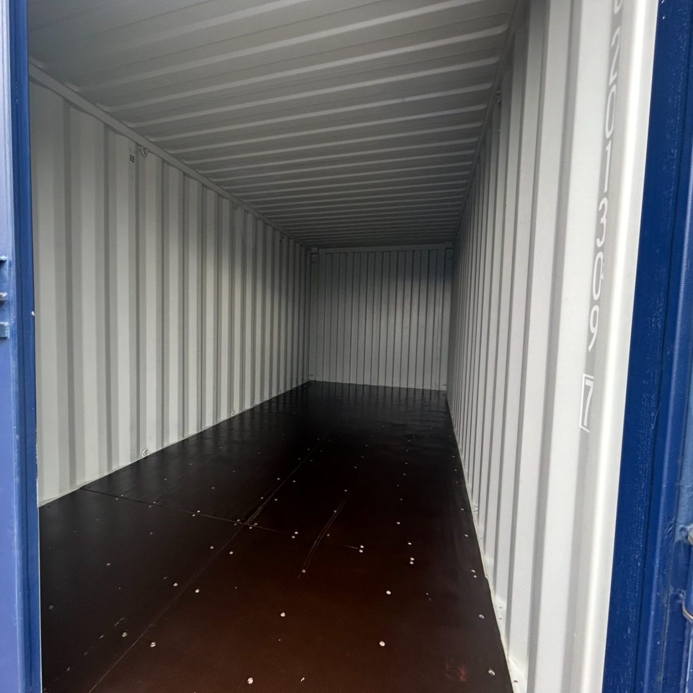 Empty shipping container interior, featuring metal walls and a brown floor.