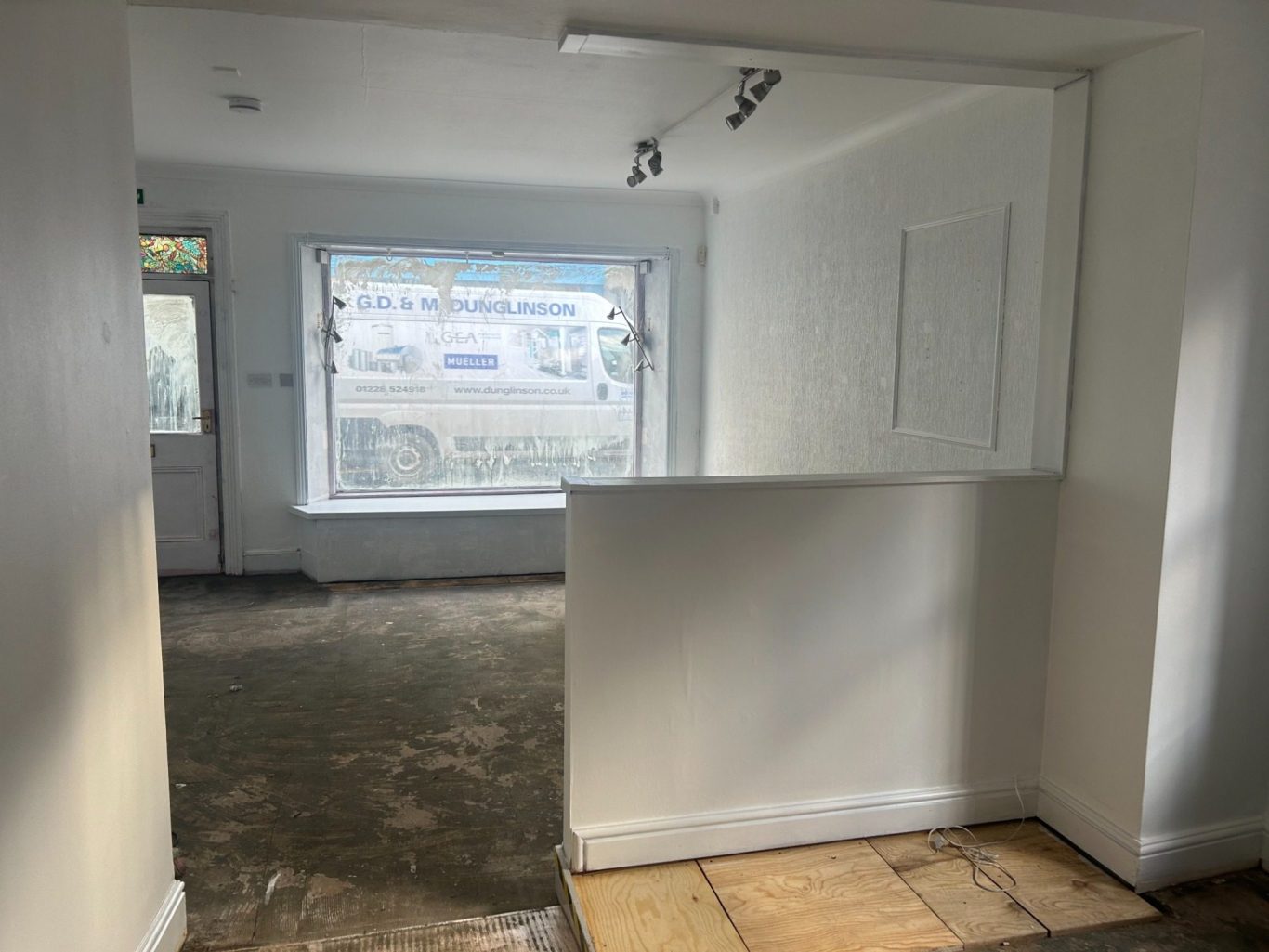 Interior view of a bright, empty room with white walls and a large window undergoing refurbishment