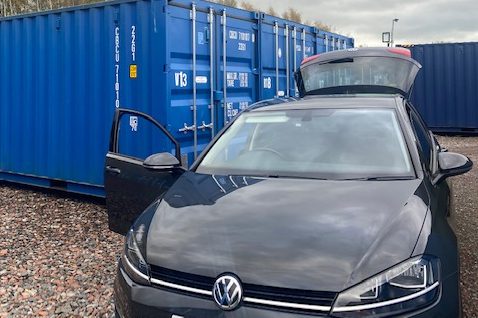 a close up of three shipping containers with a vehicle beside it