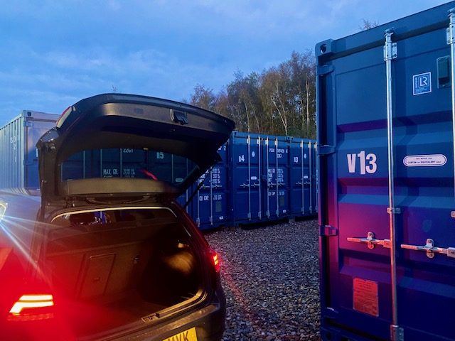 a car with its boot open at night unloading into a storage locker