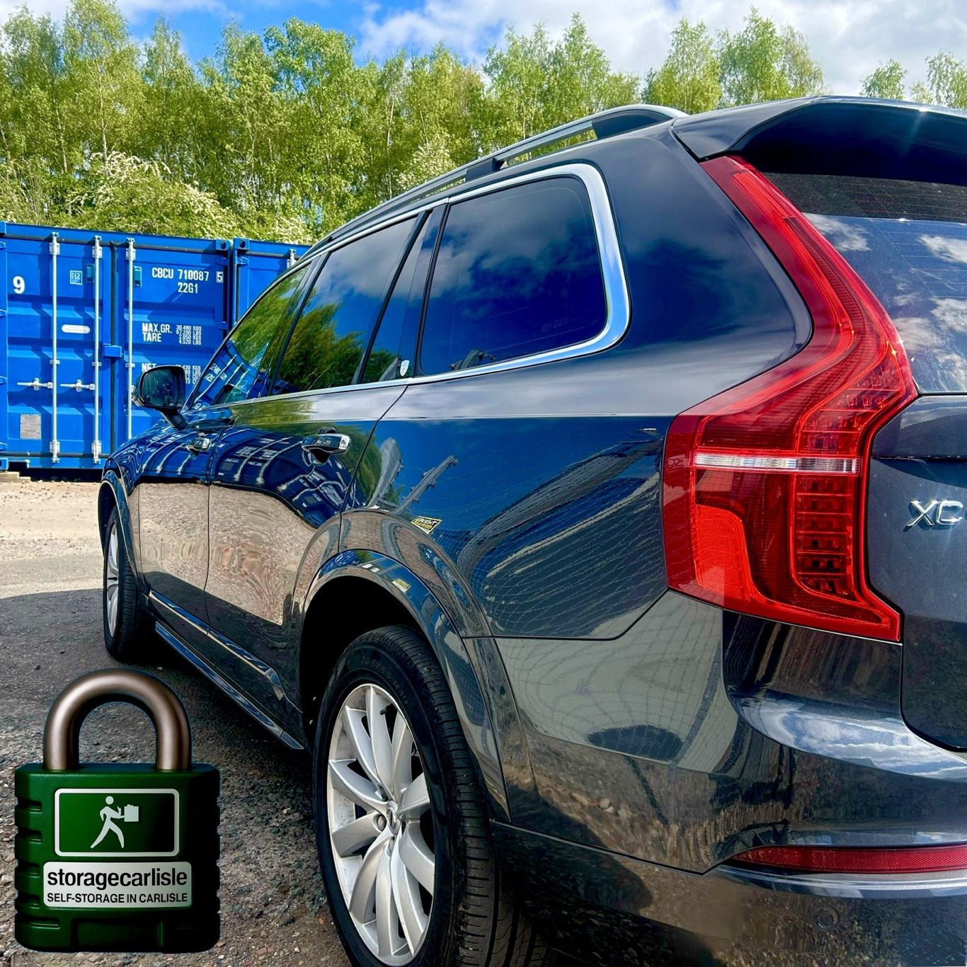 Black SUV parked beside blue shipping containers under a clear sky.