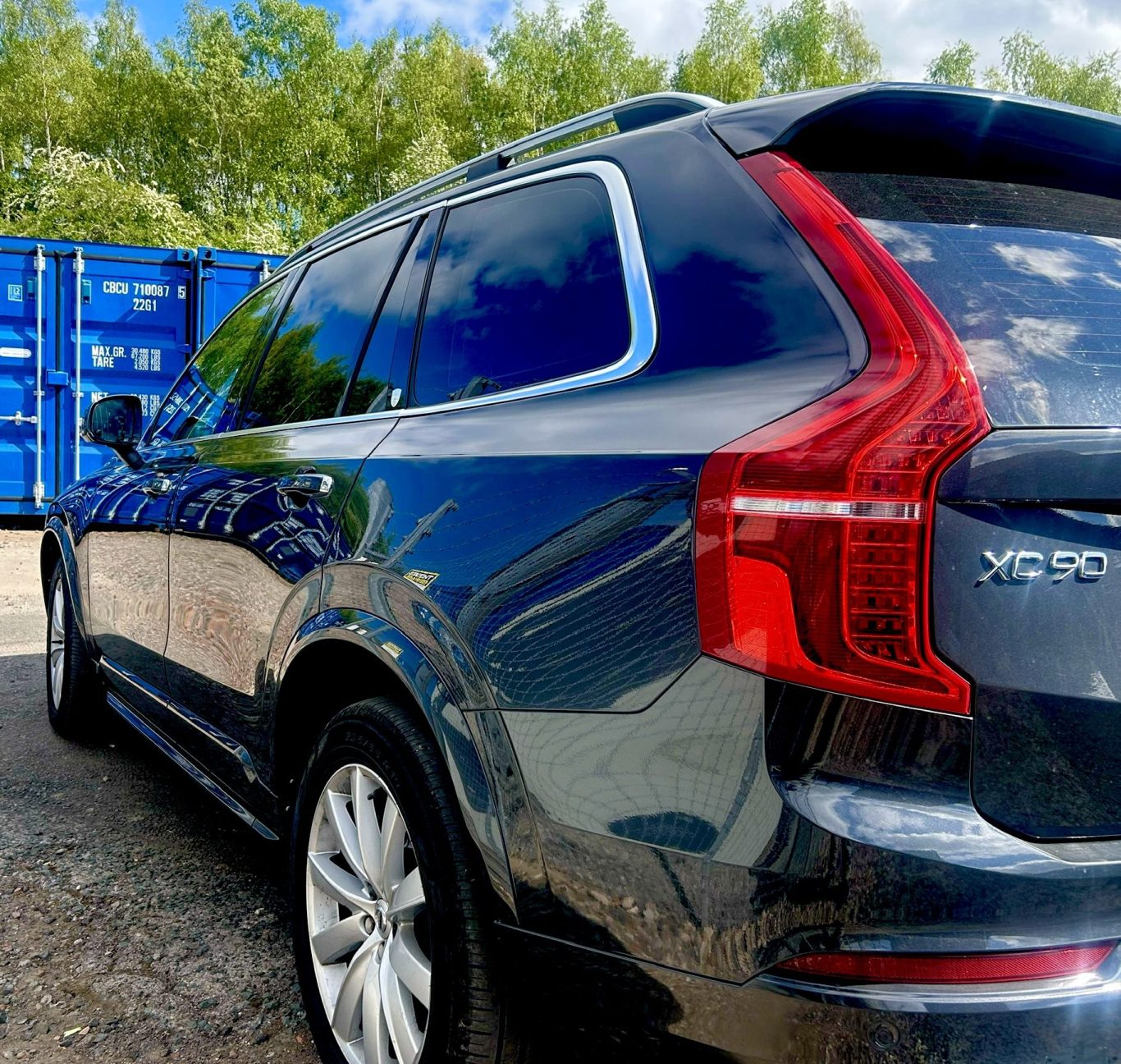 Black SUV parked beside blue shipping containers under a clear sky.