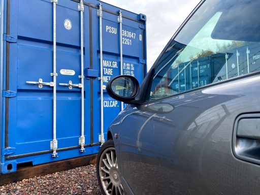 Grey car parked next to a blue shipping container.