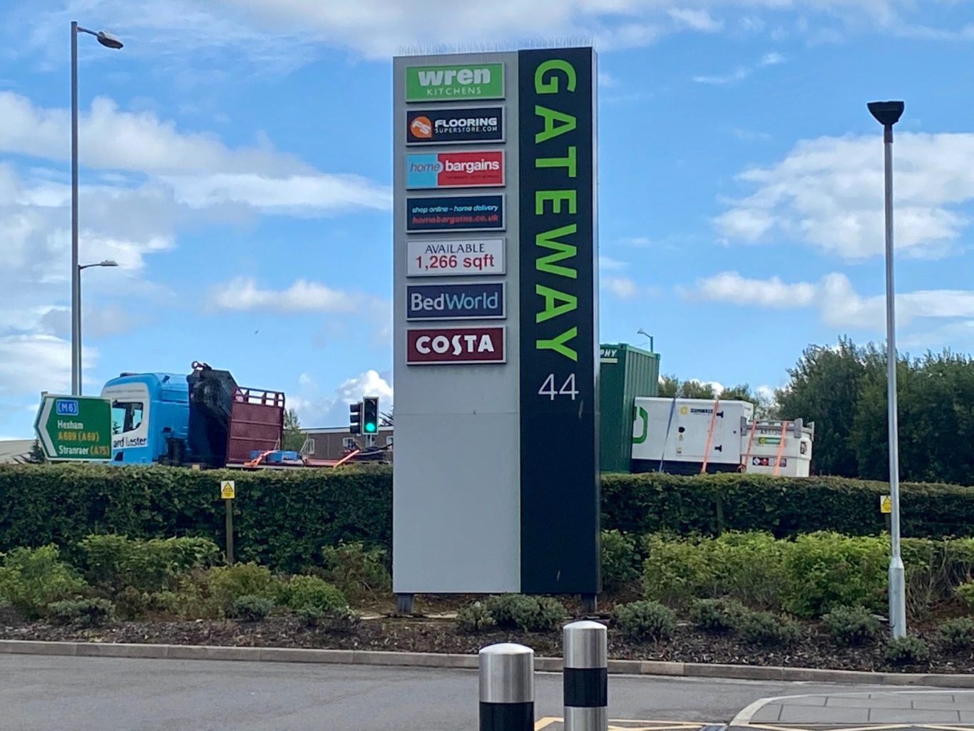Signpost for Gateway 44 near Kingstown Industrial Estate, Carlisle, with various retail logos and a blue sky background.