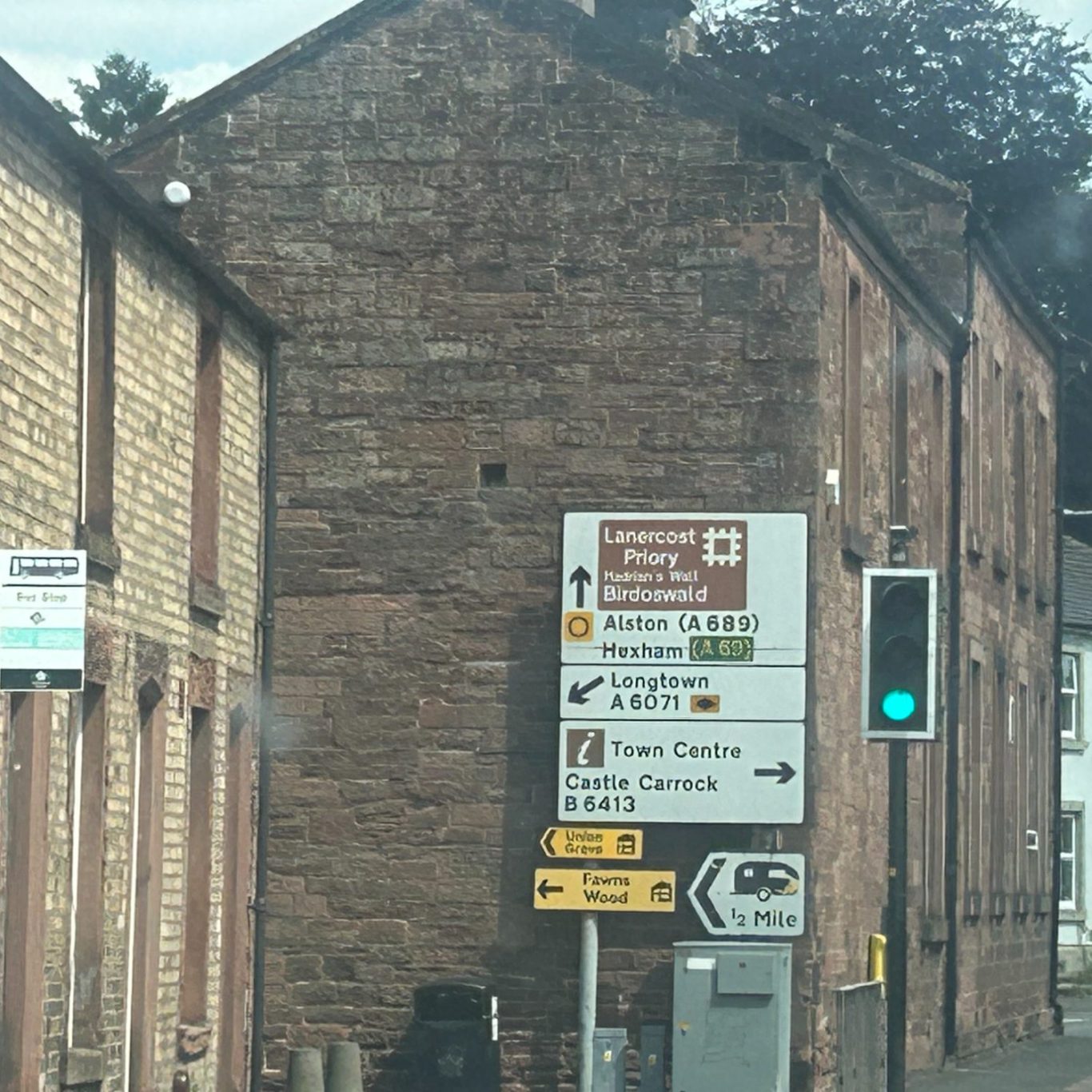 Traffic signs in Brampton, Cumbria indicating directions and information near a brick building.