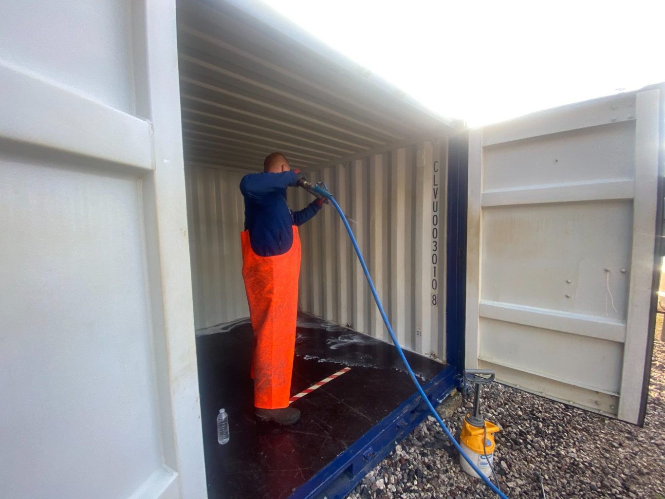 a person pressure washing the inside of a shipping container
