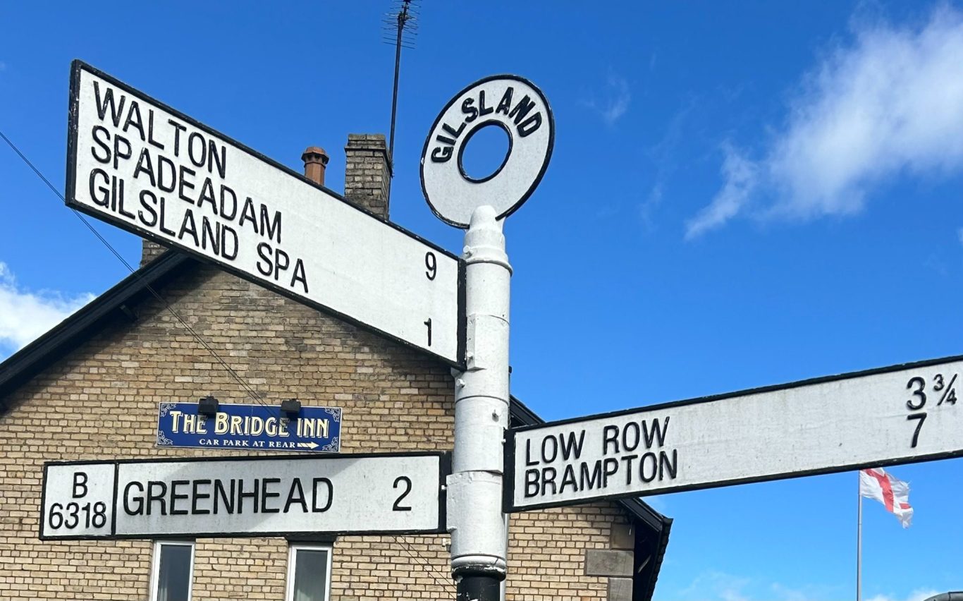Sign post in Cumbria at Gilsland Signpost displaying directions and distances to various locations, including Brampton, Low Row, Gilsland and Greenhead.