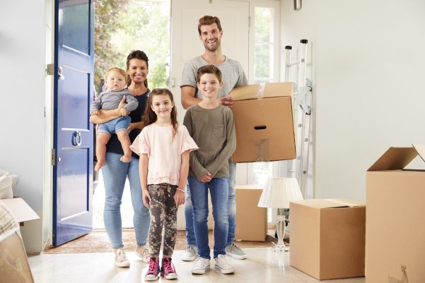smiling family opening front door to house with father carrying box