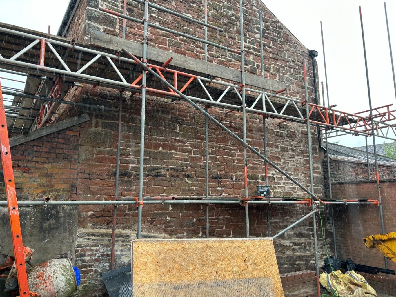 Scaffolding against a brick wall, with tools and materials on the ground.