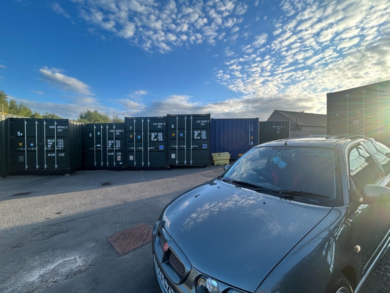 silver car parked infront of  shipping containers with a large turning circle highlighting the ease of turning on a self storage site.