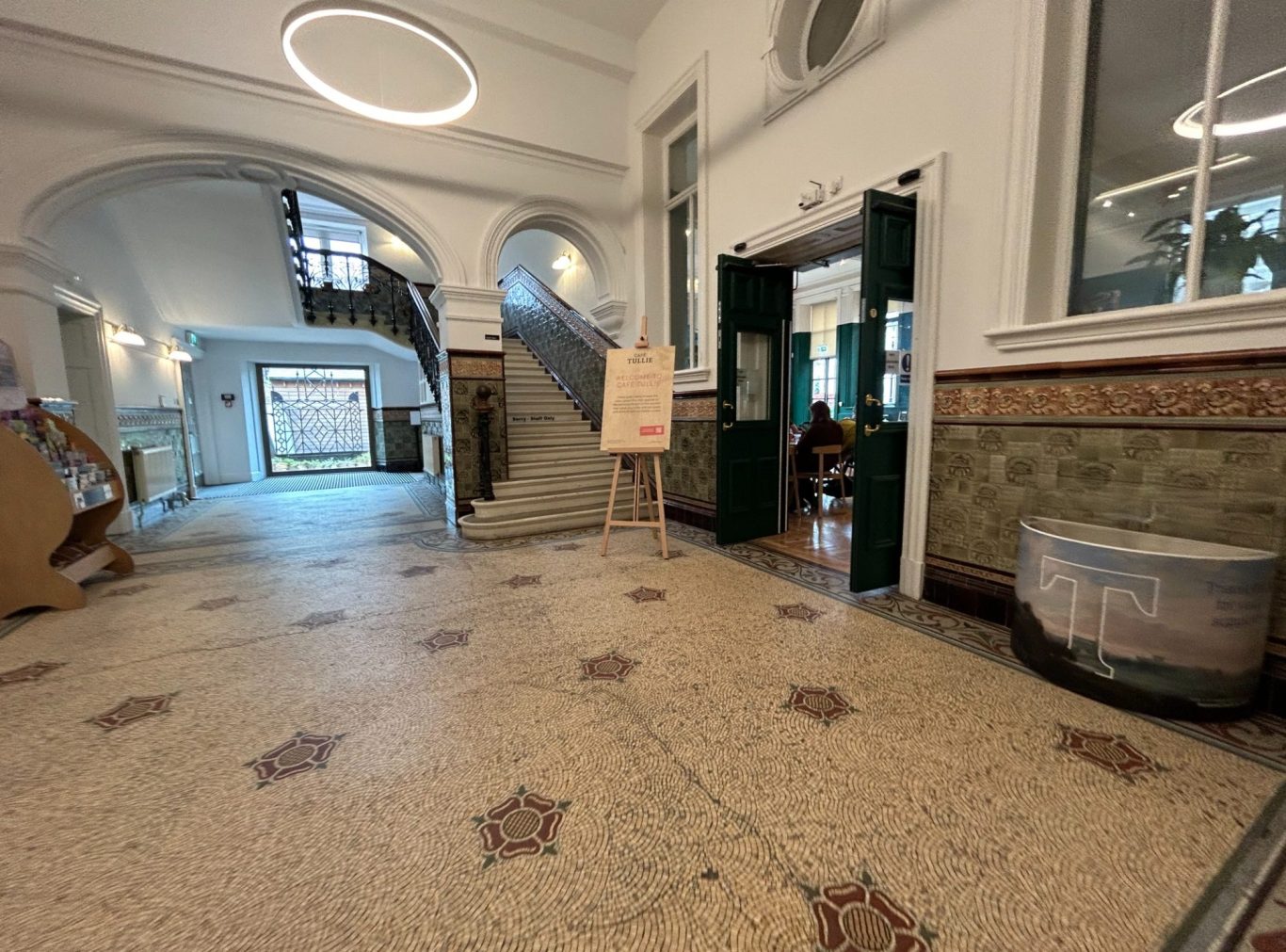 Interior view of the hallway of Tullie House Museum in Carlisle with stairs, sign, and decorative floor tiles.