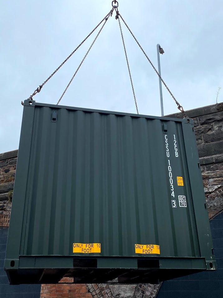 a 10 foot shipping container in the air being delivered by crane